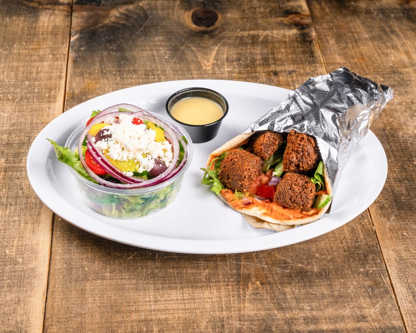 Falafel wrap with a side salad topped with feta cheese and a small cup of dressing.