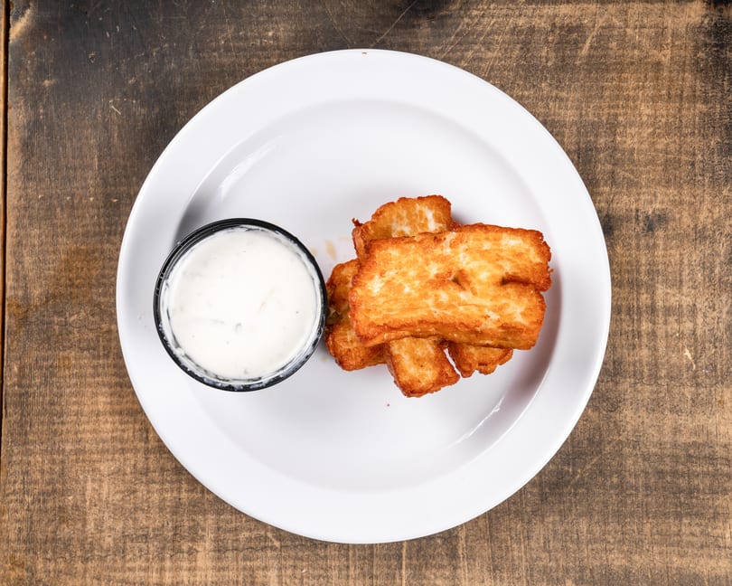 Golden-brown fried cheese curds with a side of white dipping sauce on a white plate.