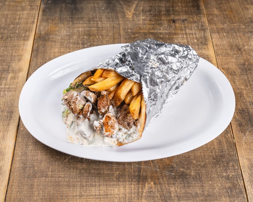 A shawarma wrap with meat, fries, and white sauce, partially wrapped in foil on a white plate.