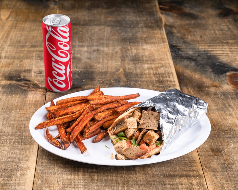 A gyro wrap with sweet potato fries and a Coca-Cola can on a white plate.